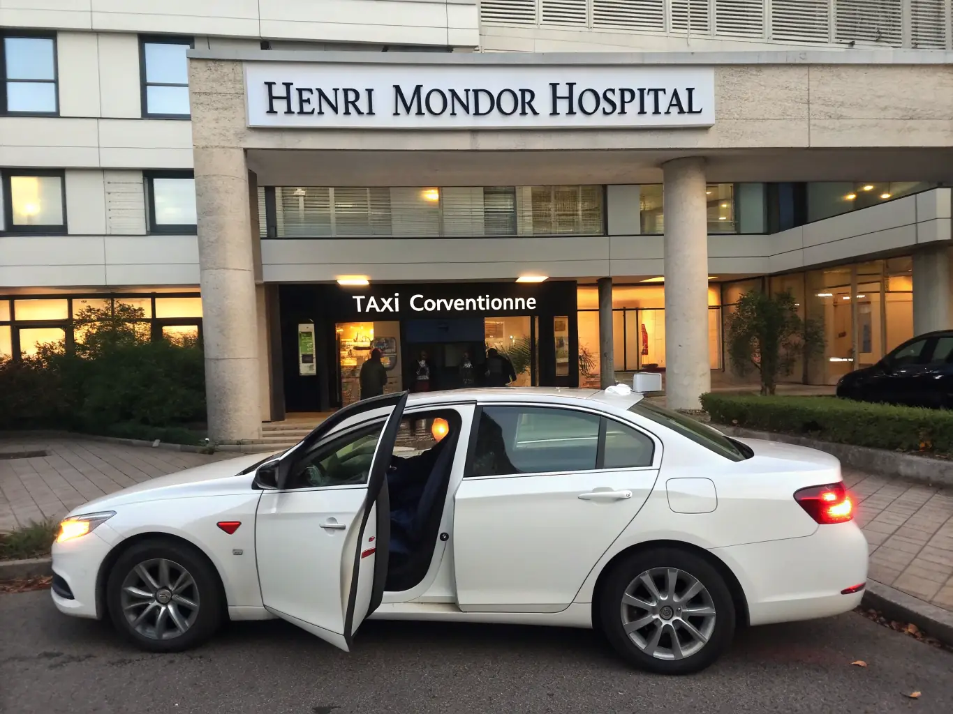 A Taxi conventionné Créteil taxi parked outside of Créteil Intercommunal Hospital, with the hospital entrance visible in the background. The scene emphasizes the taxi's proximity and availability for medical appointments.